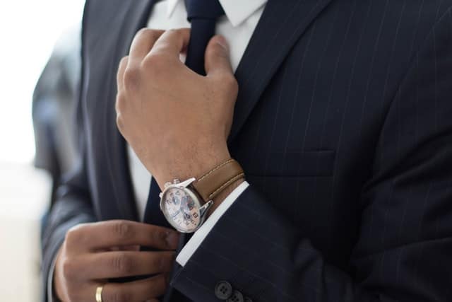 Mand med jakkesæt, ur og slips der retter slipset